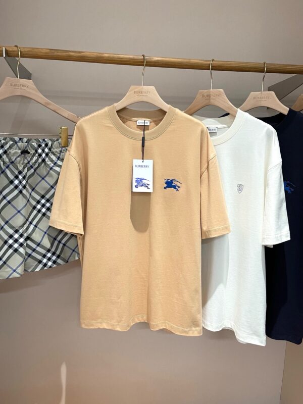 Display di t-shirt minimaliste beige, bianca, blu navy e shorts a quadri grigi e neri