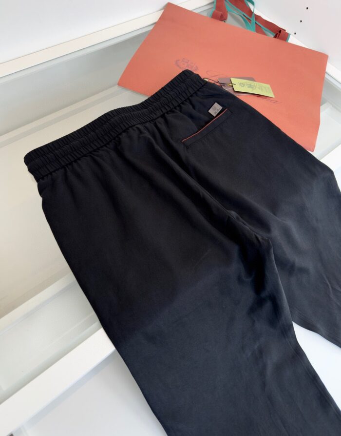 Pantaloni neri casual con elastico e tasca, sfondo con borsa arancione moderna.