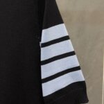 Maglione nero con dettagli a righe blu sulla manica, stile sportivo e moderno.
