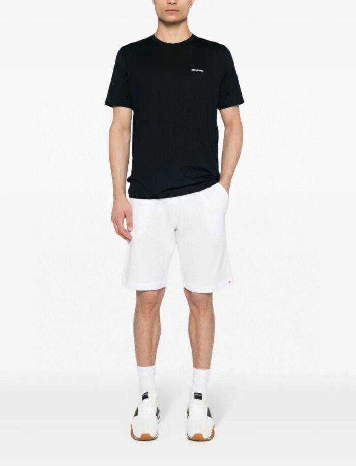 Look casual con t-shirt nera, shorts bianchi e sneakers sportive per il tempo libero.