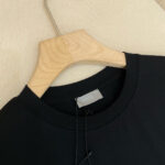 Maglietta nera casual su gancio di legno, tessuto morbido e stile minimalista elegante.