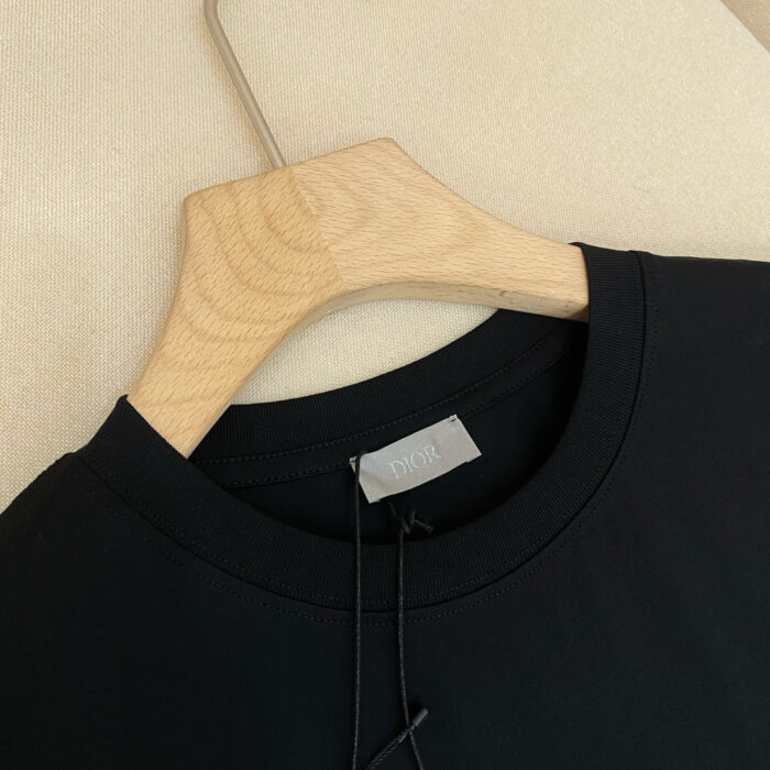 Maglietta nera casual su gancio di legno, tessuto morbido e stile minimalista elegante.