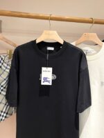 Maglietta nera casual in cotone con cartellino, esposta in negozio moderno e minimalista.