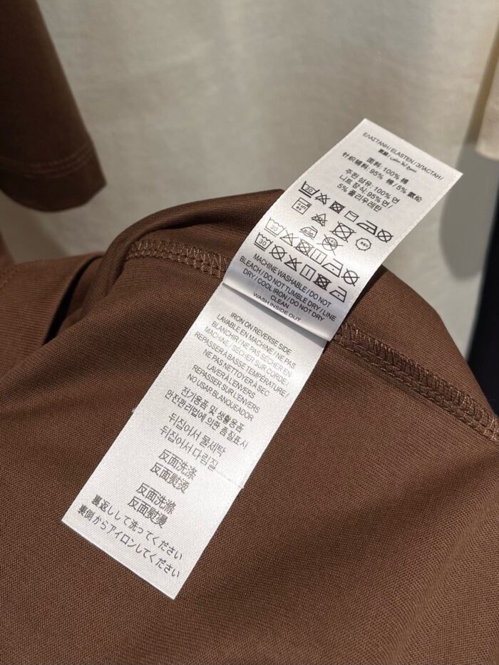 Camicia marrone in cotone con etichetta di cura e istruzioni multilingue.
