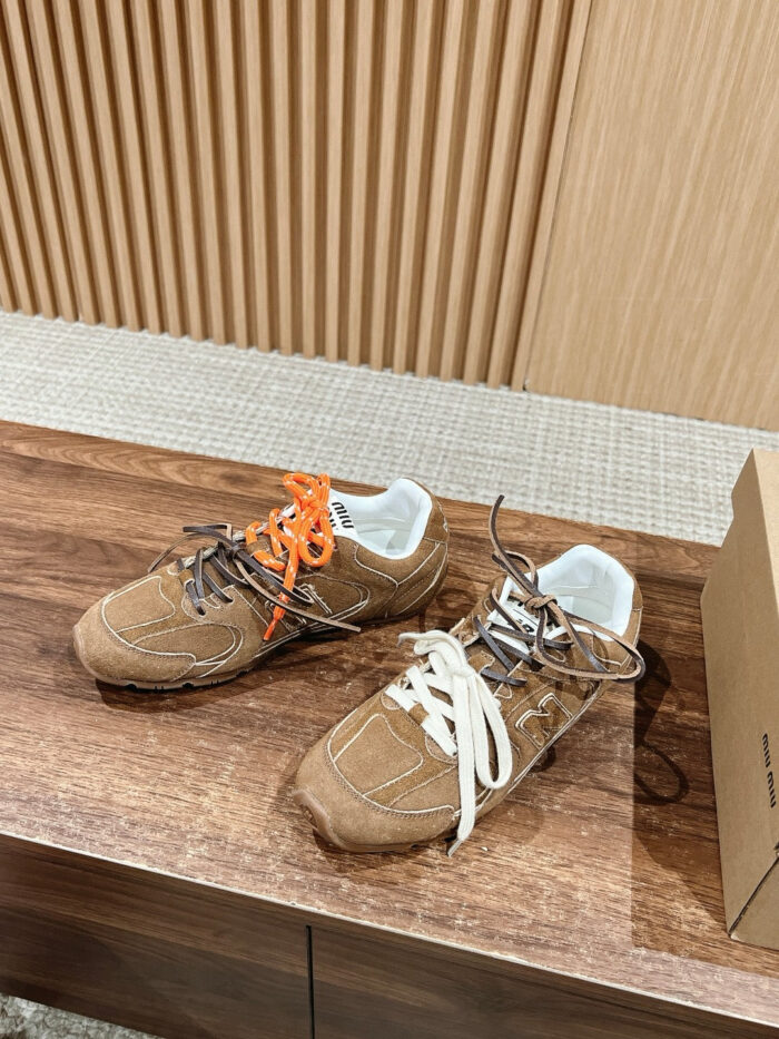 Sneakers casual in suede marrone con lacci colorati e dettagli bianchi su tavolo in legno chiaro.