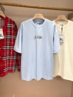 Display di abbigliamento casual con maglietta ricamata Iris, cardigan a quadri e camicia crema.