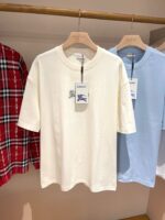 Esposizione di t-shirt casual azzurre e crema con camicia quadri rossa in negozio.