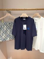 Vetrina con abbigliamento estivo casual: T-shirt navy, shorts tartan e camicia bianca elegante.