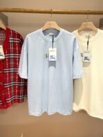 Vetrina di T-shirt casual in negozio: blu, bianca e a scacchi su appendini di legno.