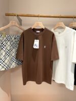 Esposizione di abbigliamento casual con T-shirt marrone, bianca e pantaloncini a quadri leggeri.