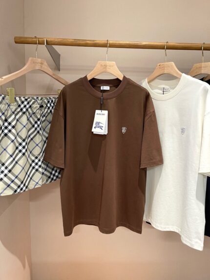 Esposizione di abbigliamento casual con T-shirt marrone, bianca e pantaloncini a quadri leggeri.