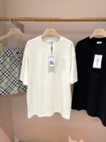 Vetrina minimalista con magliette nere, crema e shorts a quadri su appendini di legno.