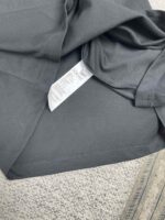 T-shirt grigio scuro con etichetta cura, tessuto sintetico e sfondo in tessuto chiaro.