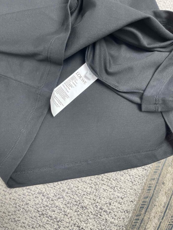 T-shirt grigio scuro con etichetta cura, tessuto sintetico e sfondo in tessuto chiaro.