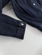 Dettaglio della manica di camicia scura con polsino con bottone in metallo elegante.