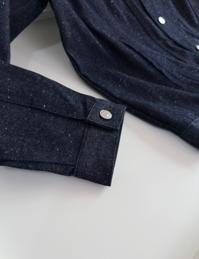 Dettaglio della manica di camicia scura con polsino con bottone in metallo elegante.