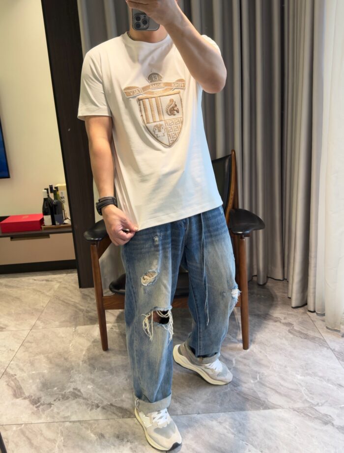 Persona con jeans distressed, maglietta bianca e sneakers bianche in uno stile casual.