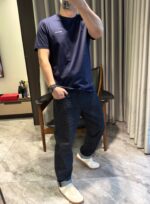 Persona casual con t-shirt navy, jeans scuri e scarpe slip-on in ambiente domestico accogliente.