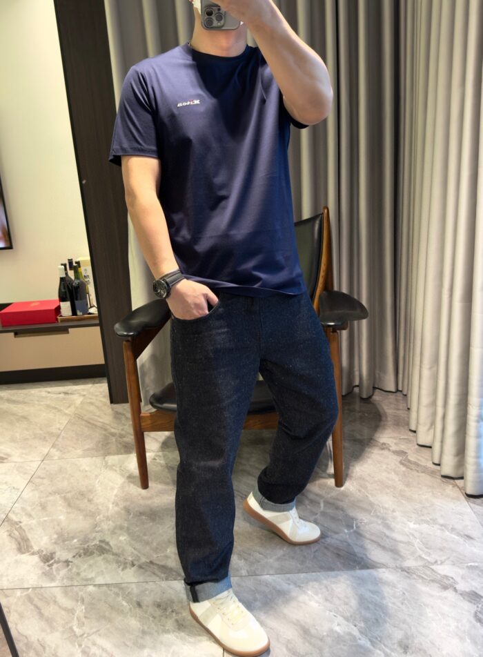 Persona casual con t-shirt navy, jeans scuri e scarpe slip-on in ambiente domestico accogliente.