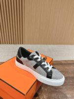 Sneaker grigia e nera con suola bianca su scatola arancione, stile casual e sportivo.