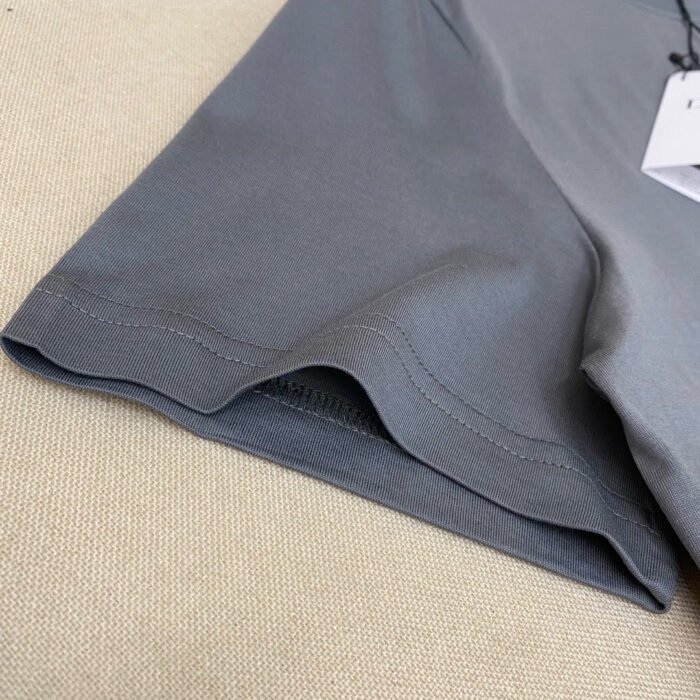 Dettaglio di orlo e cuciture di un indumento casual in tessuto leggero grigio.