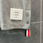 Maglietta polo grigia con etichetta moderna, bottoni metallici e dettaglio a strisce colorate.