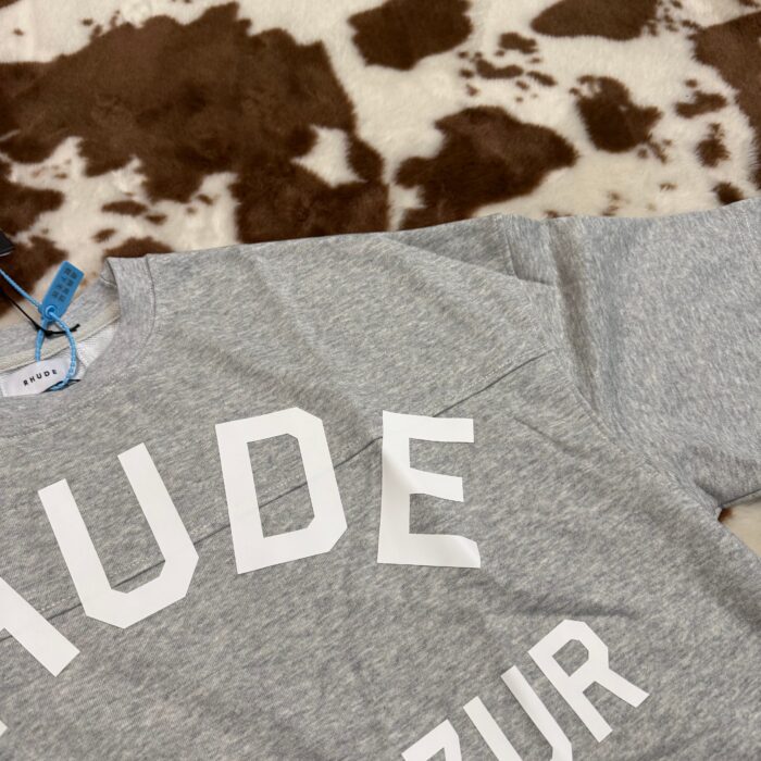 Maglietta grigia con logo NUDE su sfondo a pelo di mucca, stile moderno e casual.
