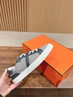 Sneaker casual grigia con dettagli navy su scatola arancione, stile minimalista e moderno.