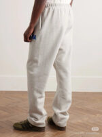 Pantaloni jogger grigi con logo blu e sneakers retro in ambiente casual e accogliente.