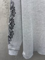 Maglietta grigia con decorazione floreale nera sulla manica, stile casual e dettagli raffinati.