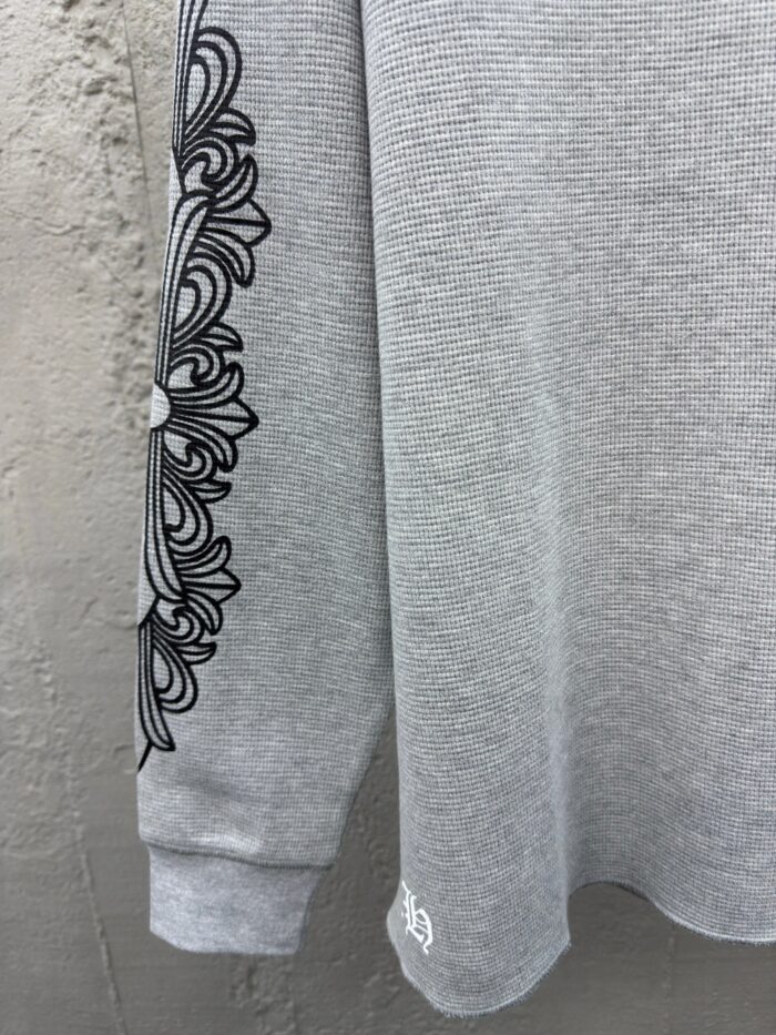 Maglietta grigia con decorazione floreale nera sulla manica, stile casual e dettagli raffinati.