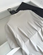 Outfit casual con maglietta grigia e pantaloni neri su superficie trasparente.