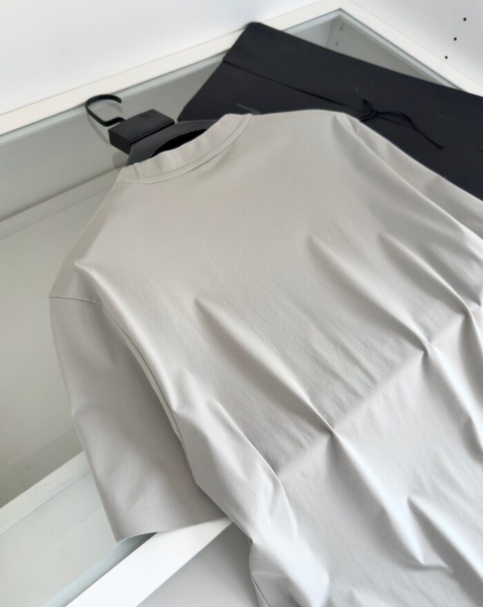 Outfit casual con maglietta grigia e pantaloni neri su superficie trasparente.