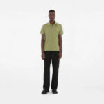 Uomo in stile casual minimalista con polo verde oliva e pantaloni neri su sfondo bianco.