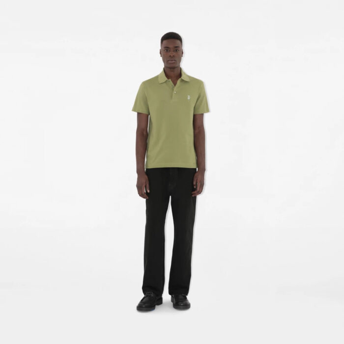 Uomo in stile casual minimalista con polo verde oliva e pantaloni neri su sfondo bianco.