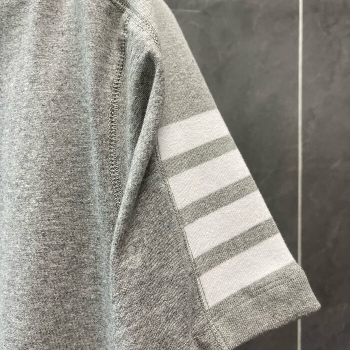 Maglietta grigia con tre strisce bianche, stile sportivo e casual, tessuto morbido e confortevole.