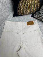 Jeans chiari a vita alta su divano elegante con tasche e patch in pelle.