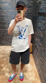 Stile streetwear casual con logo Louis Vuitton, shorts neri e scarpe colorate in ambiente moderno.