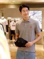 Giovane uomo sorridente in negozio di moda moderna con polo grigia e cappellino nero.