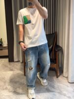 Look casual con t-shirt colorato, jeans distressed e sneakers bianche in ambiente domestico.