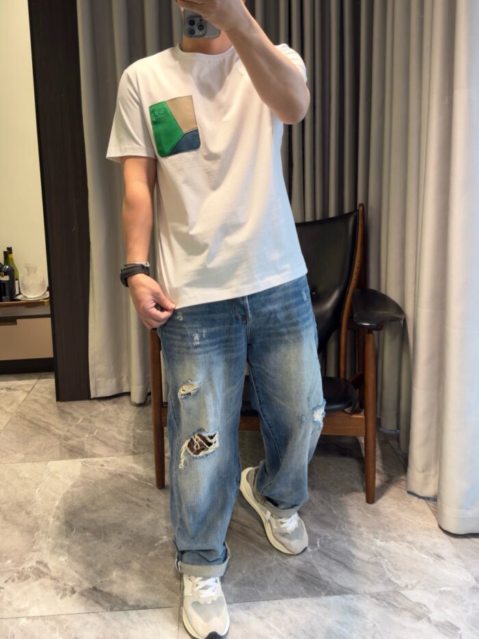 Look casual con t-shirt colorato, jeans distressed e sneakers bianche in ambiente domestico.
