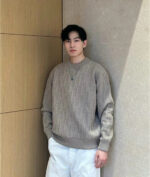 Uomo elegante in stile casual modern con sweater oversize e pantaloni bianchi in ambiente luminoso.