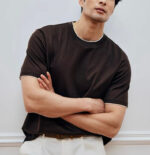 Uomo con T-shirt marrone, pantaloni chiari, stile casual e elegante, ambiente minimalista.