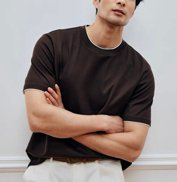 Uomo con T-shirt marrone, pantaloni chiari, stile casual e elegante, ambiente minimalista.