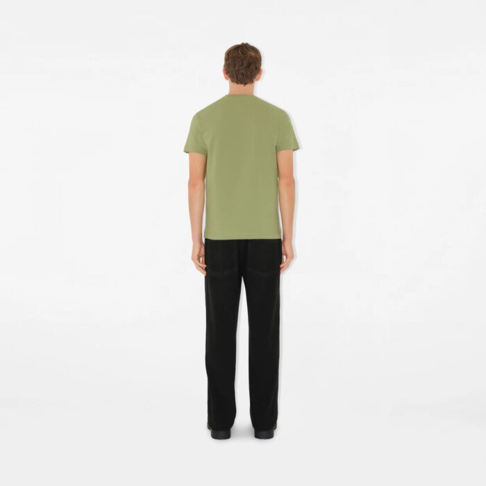 Uomo di spalle in outfit casual verde oliva e pantaloni neri su sfondo bianco minimalista.