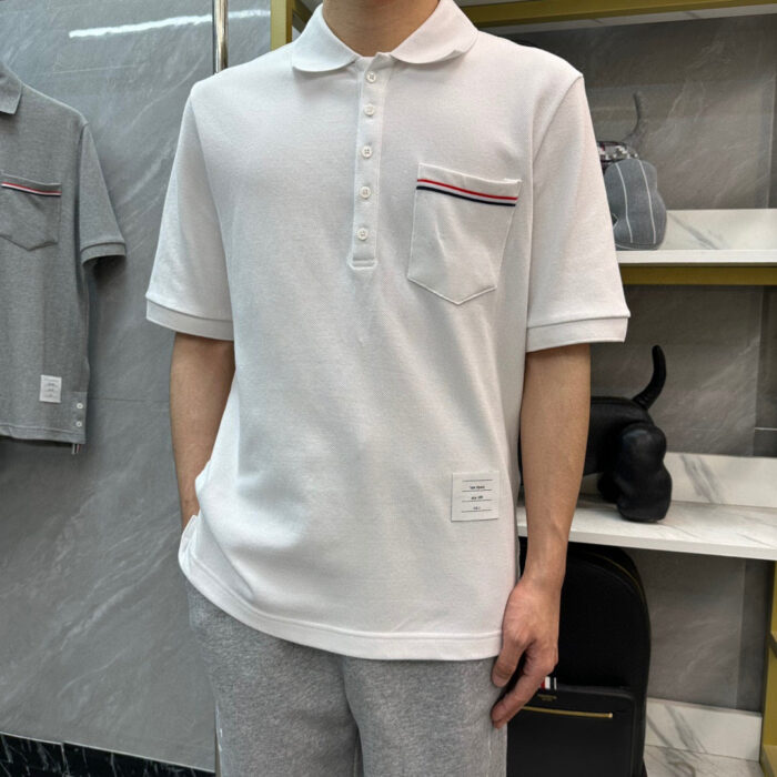Maglietta polo bianca casual con tasca a righe, pantaloni grigi, stile moderno e confortevole.
