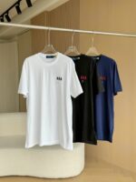 T-shirt minimalisti bianco, nero e blu navy su stendino moderno in ambiente luminoso e elegante.