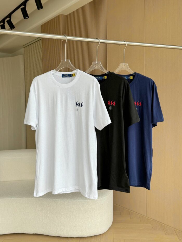 T-shirt minimalisti bianco, nero e blu navy su stendino moderno in ambiente luminoso e elegante.