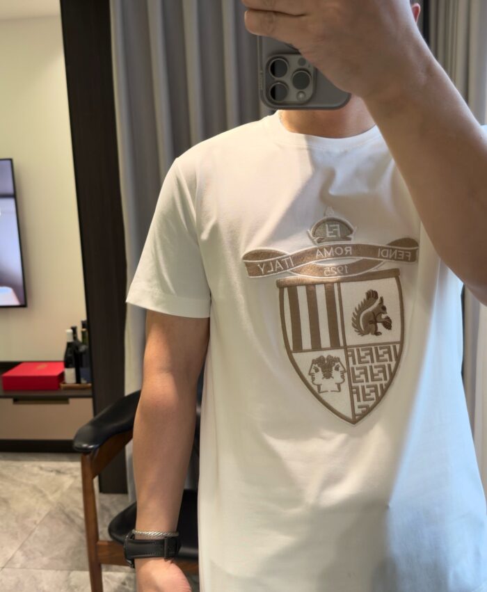 Selfie con maglietta bianca e emblema dorato in ambientazione moderna e minimalista.