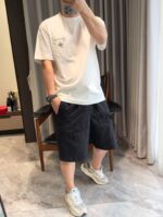 Donna in outfit casual con t-shirt, shorts scuri e sneakers bianche in bagno con specchio.
